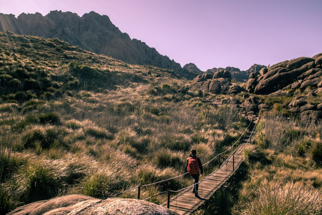 ponte em trilha bem sinalizada com pessoa caminhando e vendo a vista para o pico das agulhas negras