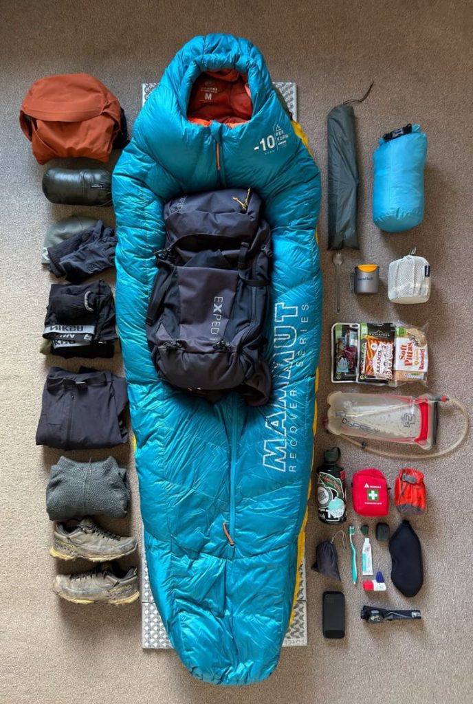 Equipamentos essenciais organizados para trilha: mochila, lanterna, água, corta-vento, primeiros socorros e mapa.